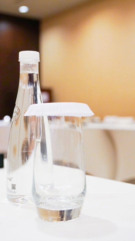 Two tables, water bottle, two glasses, white tablecloth, black box.